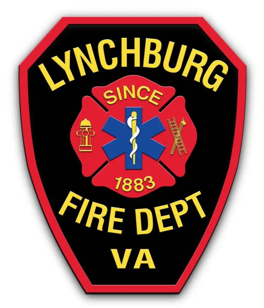 A badge-shaped Lynchburg Fire Department emblem with a black background and red border. The text reads "Lynchburg Fire Dept VA" with a central red maltese cross containing symbols: a hydrant, the Star of Life, and a ladder with an axe. "Since 1883" is written in gold.