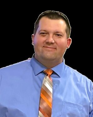 A man with short dark hair is smiling faintly. He is wearing a blue dress shirt and a striped tie with orange, white, and brown colors. The background is entirely black.